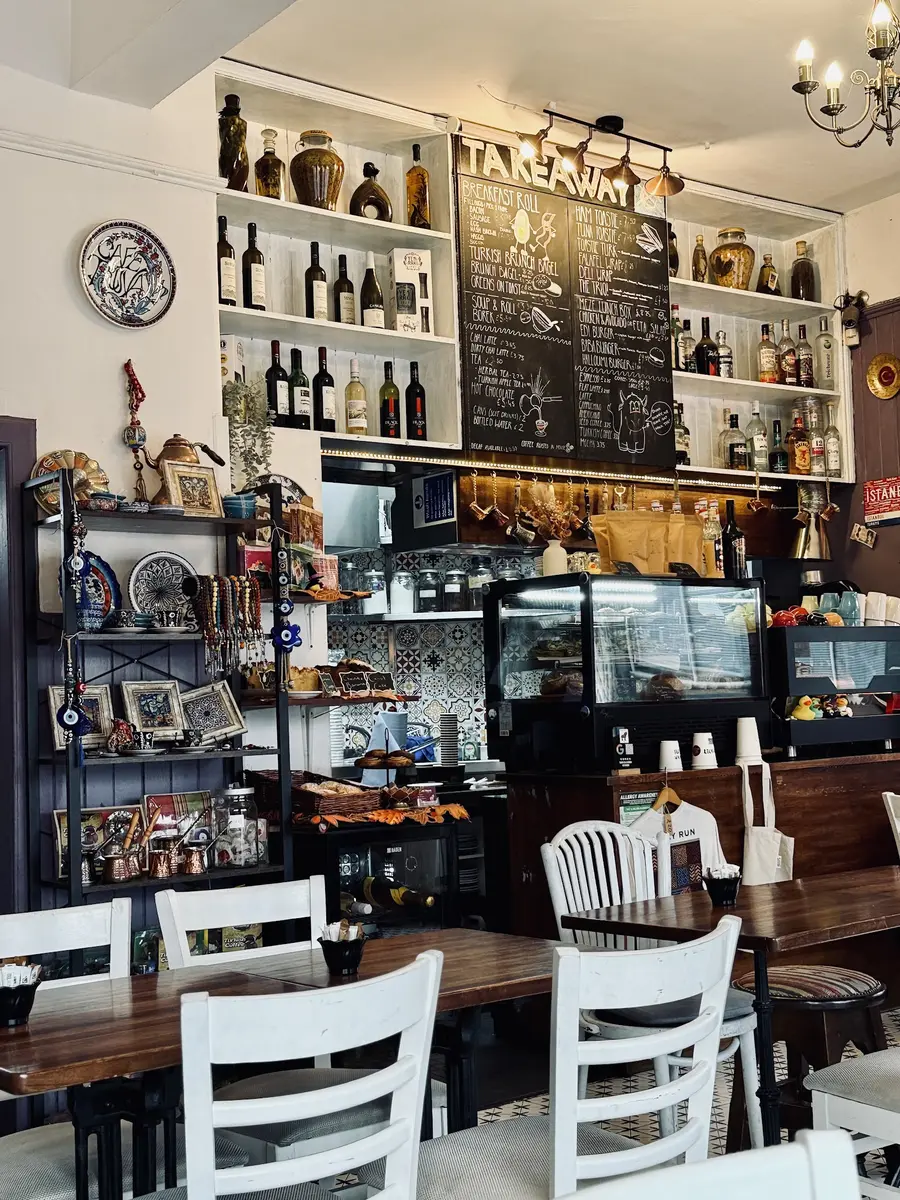 Inside Cafe Truva — takeaway chalkboard menu, shelves of wine and rakı, Turkish ceramics and evil-eye charms