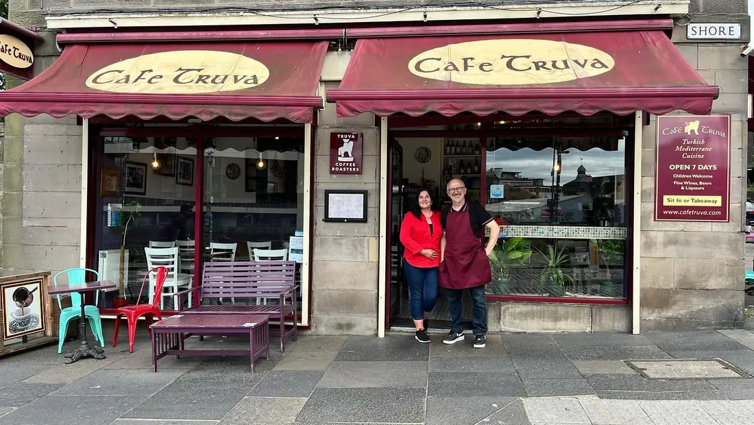 The owners standing together outside Cafe Truva under the burgundy awnings
